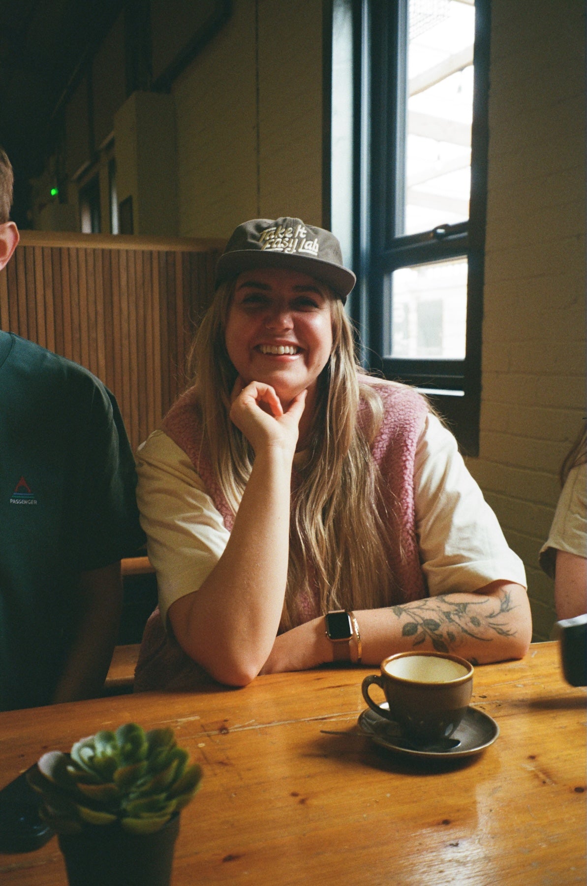 Person sitting at a table with a cup of coffee, wearing a cap and a watch.