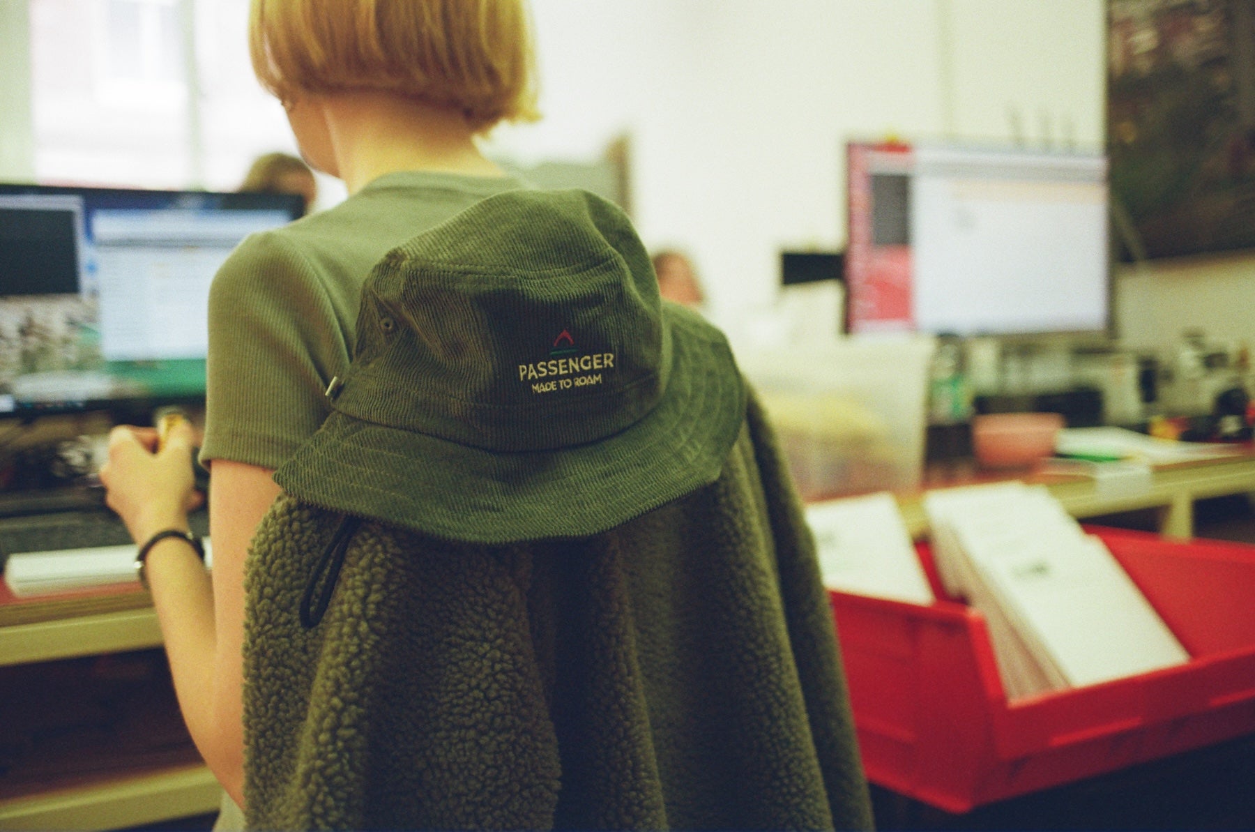 Person wearing a green top with a green cord hat on the back of her chair, showing 'Passenger' branding in an office setting.