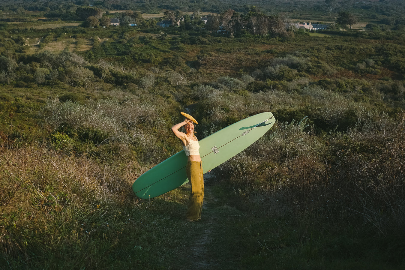 Person holding a green surfboard and French baguette in a grassy field